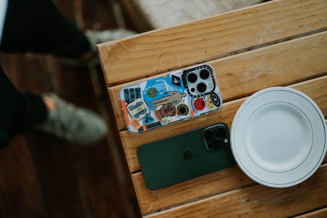 Top view of smartphones on a wooden table, showcasing a colorful case design and an empty plate.