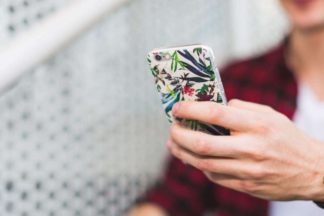 A person holds a smartphone with a decorative floral case, wearing a red plaid shirt.